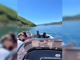 A lively group enjoys a sunny day on a boat, capturing the beautiful lake scenery — perfect for memorable outings with friends.