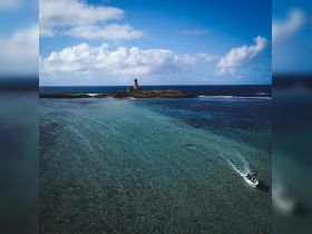 A scenic view of a boat navigating through clear waters near an island with a lighthouse, showcasing the beauty of coastal adventures.