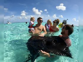 A joyful family interacts with a stingray in shallow waters, creating unforgettable memories during their aquatic adventure.