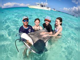 A memorable encounter as children interact with a stingray in shallow waters, showcasing the thrill of wildlife experiences in the Bahamas.
