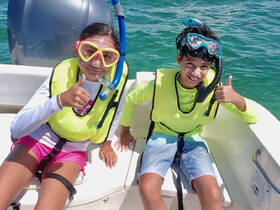 Two children excitedly prepare for snorkeling on a boat, showcasing their gear and enthusiasm for underwater adventures.