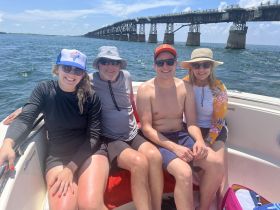 A cheerful group of friends enjoys a sunny day on the water, posing together on a boat with a scenic bridge in the background — perfect for memorable outings and adventures.