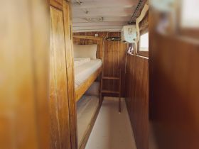 Cozy interior of a boat cabin featuring bunk beds and wooden paneling, perfect for comfortable overnight stays on the water.