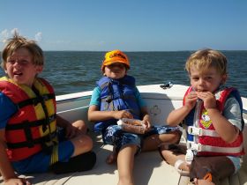 Three kids enjoy snacks on a boat, showcasing a fun family outing on the water.