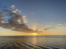 A breathtaking sunset over the calm ocean, with clouds reflecting the warm hues of the evening sky — a perfect backdrop for serene moments on the water.
