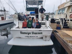 A cheerful group poses on the deck of the 'Kamryn Dawson' in Long Beach, CA, capturing a memorable moment before their boating adventure.