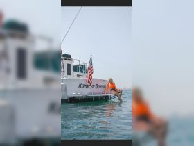 A woman relaxes on the edge of a boat named 'Kamryn Dawson' in Long Beach, enjoying the sun and water — a perfect scene for summer outings and leisure on the water.