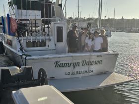 A cheerful group poses aboard the 'Kamryn Dawson' fishing boat, capturing a memorable moment at the marina — perfect for family outings and fishing adventures.