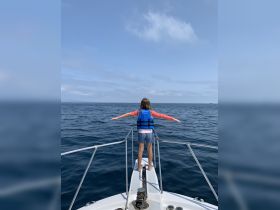 A young girl stands confidently at the bow of a boat, arms outstretched, embracing the ocean breeze — a perfect moment of adventure on the water.