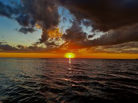 A stunning sunset over the ocean, with vibrant colors reflecting on the water's surface — a perfect backdrop for evening boat cruises.