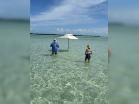 A couple enjoys a sunny day standing in shallow, crystal-clear waters under an umbrella, perfect for a relaxing beach getaway.