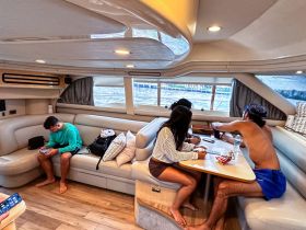 A cozy interior of a boat featuring guests relaxing and engaging in activities at the dining table, showcasing the comfortable cabin space perfect for socializing.