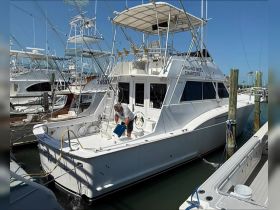 A fishing charter boat is docked with a crew member preparing for the day. The clear blue sky and marina setting highlight the boat's features.