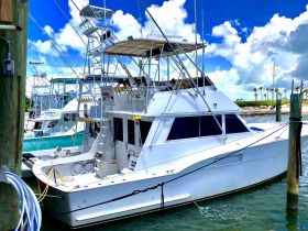 A sleek yacht docked at the marina, showcasing its impressive structure against a backdrop of blue skies and fluffy clouds.