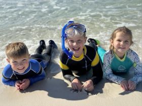 Three children enjoy a fun day at the beach, equipped with snorkeling gear and playing in the shallow water — a perfect family-friendly adventure.