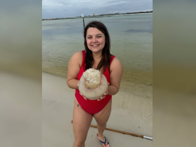 A young woman holds a jellyfish while smiling on the beach, showcasing a unique human-animal interaction in a coastal setting.