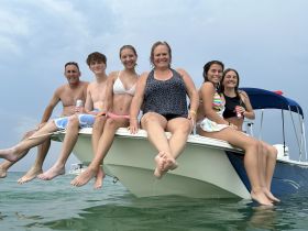 A joyful group of family and friends enjoys a fun day on the water, sitting on the bow of a boat while splashing in the waves — perfect for summer adventures.