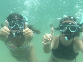Two friends enjoy snorkeling underwater, giving thumbs up in a vibrant aquatic setting — a perfect snapshot of adventure and fun in the water.