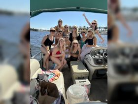 A lively group of friends celebrates aboard a pontoon boat, enjoying drinks and sunshine — perfect for a fun day on the water.