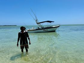 A person stands in shallow water near the fishing boat 'Maria', enjoying a sunny day at the beach — a perfect setting for fishing adventures and water activities.