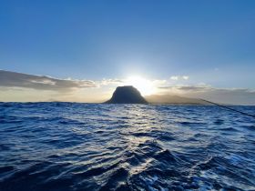A breathtaking sunset view over a distant island, showcasing the serene beauty of the coastline and the tranquil waters — perfect for nature lovers and sunset enthusiasts.