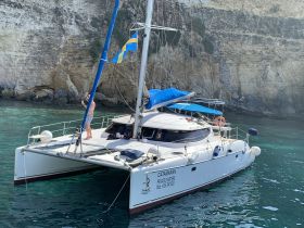 A person enjoys the stunning views from a catamaran, showcasing the beautiful turquoise waters and rocky cliffs — perfect for adventure seekers and sailing enthusiasts.