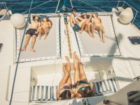 A group of friends relaxes and sunbathes on the deck of a catamaran, enjoying a perfect summer day on the water.