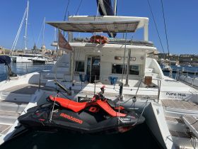 A sleek Sea-Doo jet ski is showcased on the deck of the Pupa Mia yacht, docked in a vibrant marina — perfect for water sports enthusiasts.