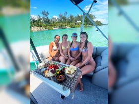 Four friends enjoy a delicious spread of snacks and drinks on a boat, perfect for a fun day on the water in a tropical paradise.