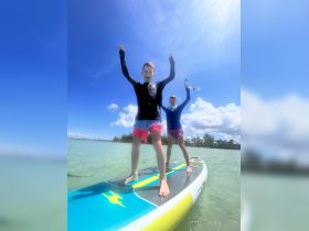 Two children joyfully paddleboard in shallow waters, showcasing the fun of water activities and adventure on a sunny day.