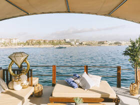 A beautifully arranged lounge area on a boat, featuring elegant decor and a stunning view of the coastline, perfect for relaxation and social gatherings.