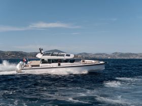 A sleek speedboat glides through the water, showcasing its elegant design and performance against a picturesque backdrop of hills and clear skies.