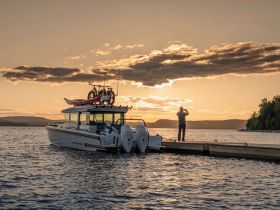 A person captures the stunning sunset while standing on a dock beside a boat, creating a picturesque moment perfect for nature lovers and photography enthusiasts.
