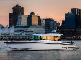 A sleek yacht glides through the water against a stunning city skyline at sunset, showcasing modern design and elegance.
