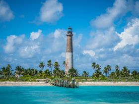 A stunning view of a historic lighthouse surrounded by palm trees and turquoise waters, showcasing the beauty of a tropical coastline.