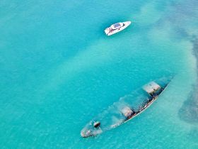 An aerial view captures a stunning contrast between a sunken wreck and a nearby boat cruising through the vibrant turquoise waters, showcasing the beauty of marine exploration.