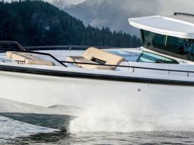 A sleek speedboat cuts through the water, showcasing its elegant design and powerful performance against a backdrop of mountains.