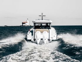A stunning view of a yacht cruising through the water, leaving a wake behind, with a lighthouse in the background — perfect for showcasing luxury boating experiences.