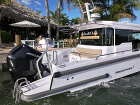 A sleek AXOPAR boat docked near a vibrant waterfront restaurant, showcasing luxury boat charters in a tropical setting.