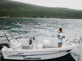 A man stands on a fishing boat, enjoying a day on the water surrounded by scenic hills — perfect for fishing enthusiasts and outdoor adventures.