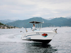 A fisherman navigates a boat through calm waters, showcasing the beautiful mountainous backdrop — perfect for fishing adventures and scenic tours.