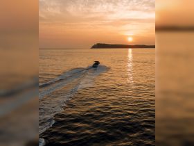 A stunning aerial view of a boat cruising at sunset, leaving a trail in the shimmering water — perfect for showcasing serene evening boat rides.