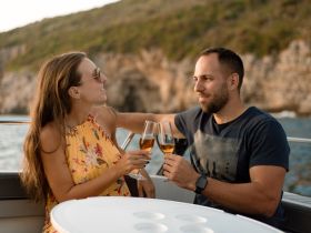 A couple enjoys a toast with cocktails on a boat, surrounded by stunning coastal scenery — perfect for romantic sunset cruises.