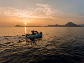 A scenic sunset view of a boat cruising on calm waters, with an island silhouette in the background — perfect for capturing memorable moments on the water.