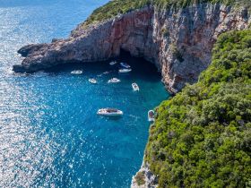 A stunning aerial view of multiple boats anchored near a picturesque coastal cave, showcasing the beauty of island boating adventures.