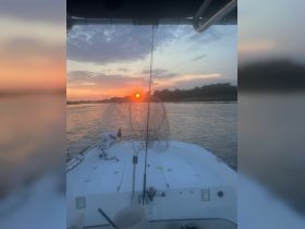 A serene sunset view from the bow of a boat, featuring fishing gear and calm waters — perfect for a relaxing evening on the water.