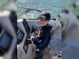 A young boy smiles while steering the helm of a boat, showcasing the excitement of learning to navigate on the water.