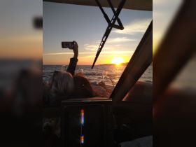 Guests enjoy a beautiful sunset aboard a boat, capturing the moment with cocktails in hand — a perfect setting for memorable celebrations on the water.