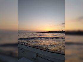 A serene sunset view from the deck of a boat, showcasing calm waters and a distant shoreline — perfect for peaceful evening cruises.