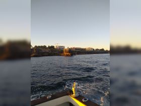 A scenic view from a boat showcasing the rugged coastline and buildings in the distance, perfect for capturing the beauty of maritime adventures.